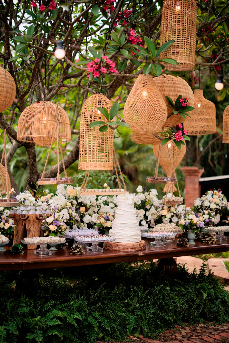 Mesa de bolo com luminárias de palhinha, com decoração rústica, samambaias e flores brancas em um espaço para casamento no interior , em Indaiatuba